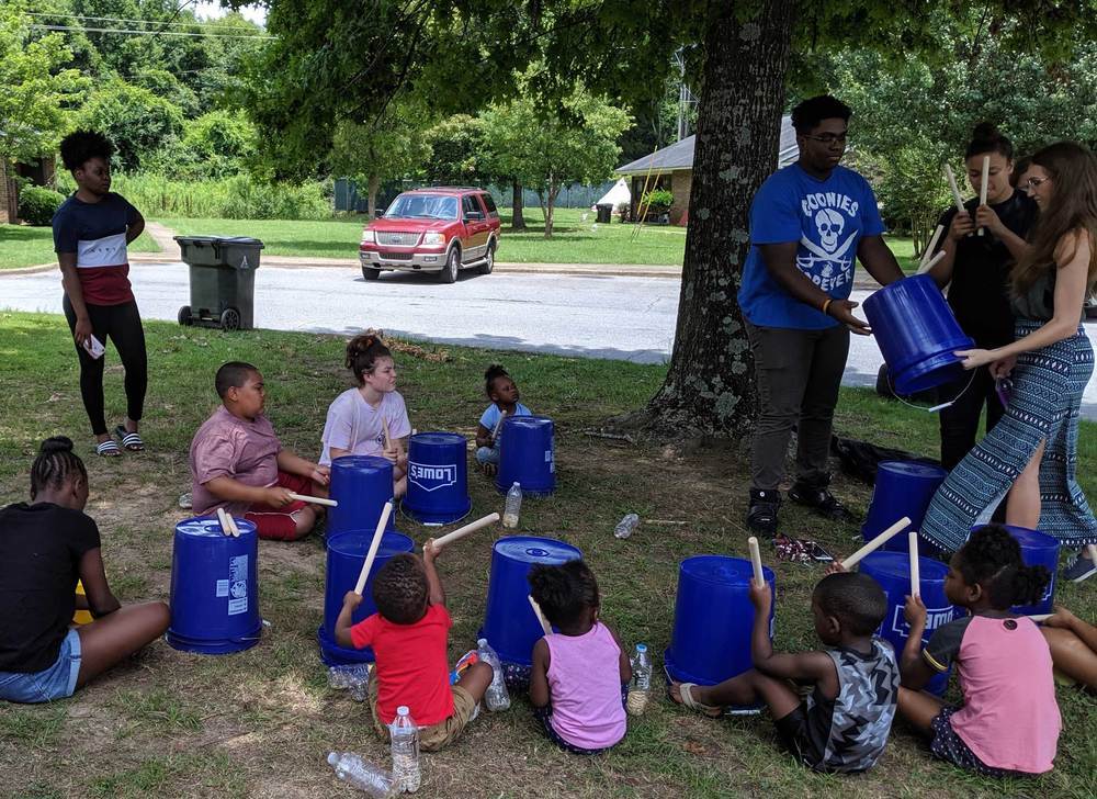 Group of kids and volunteers drumming at summer feeding
