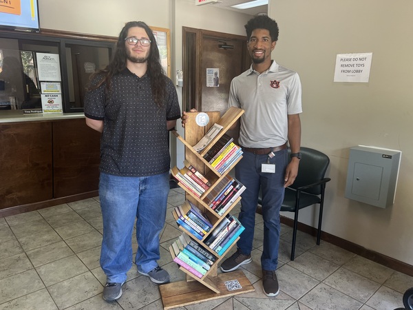 Austin Pearson of LCLC is standing with AHA\'s AJ Harris and the new pop-up wooden bookshelf library for the Ridgecrest Admin Office. 