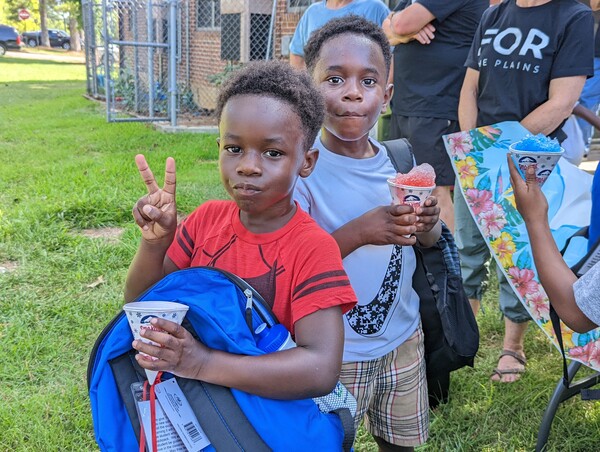 Young boys are seen holding new backpacks and snow cones, while one is giving the peace sign.