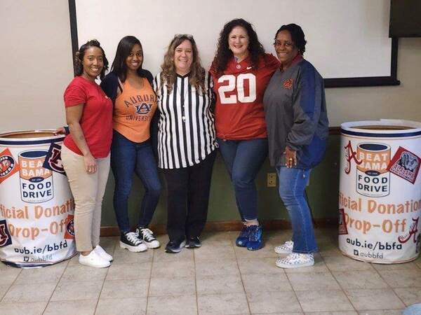 Auburn Staff posing beside Beat Bama Food Drive Donation containers.