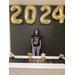 graduate in jeans and black shirt under the 2024 balloons and behind the decorate table