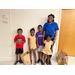 Group of elementary aged youth posing up against wall with their new school supply bags on the floor beside them